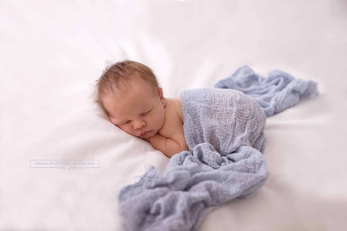 Neugeborenenpose mit blauen Tuch verschönert beim Shooting mit Sabrina Zisch-Ortner