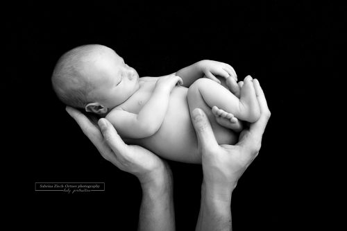neugeborene Junge in Papas Händen auf schwarzen Decke am Beanbag