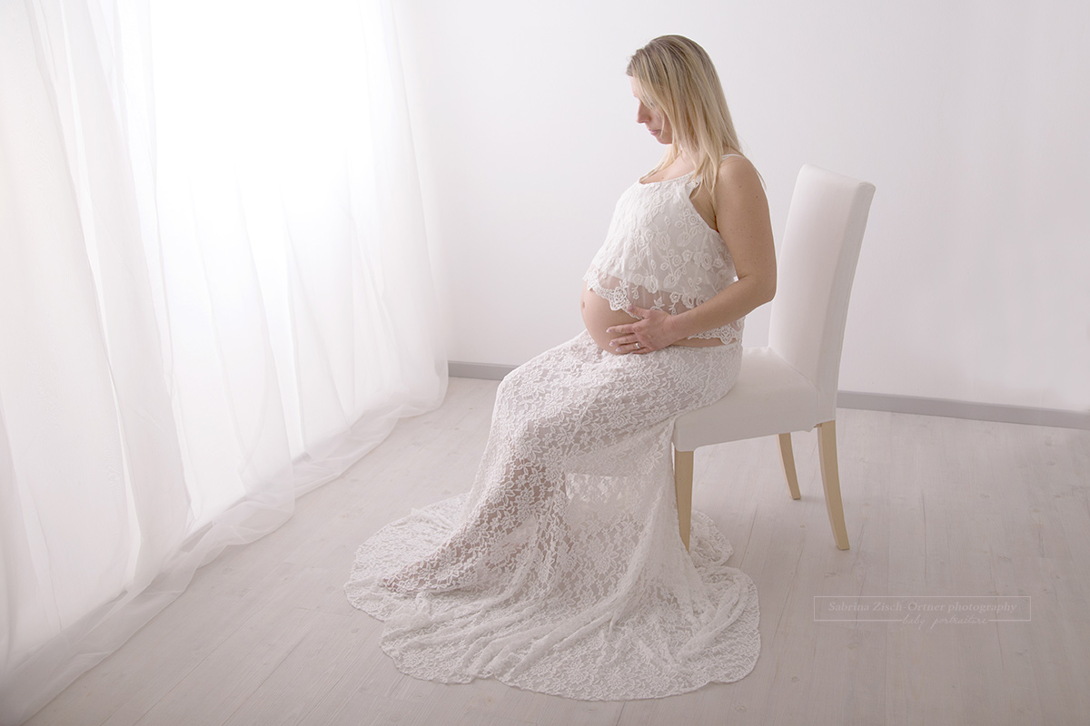 schwangere mit einem spitzen Babybauchrock sitzend auf einem weißen Sessel