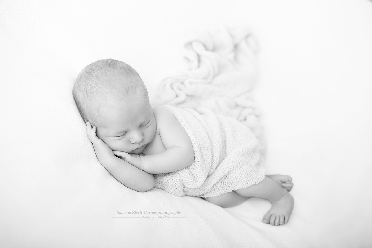 Baby liegt seitlich auf dem Beanbag mit den Händen unter dem Kopf und einem Tuch bedeckt