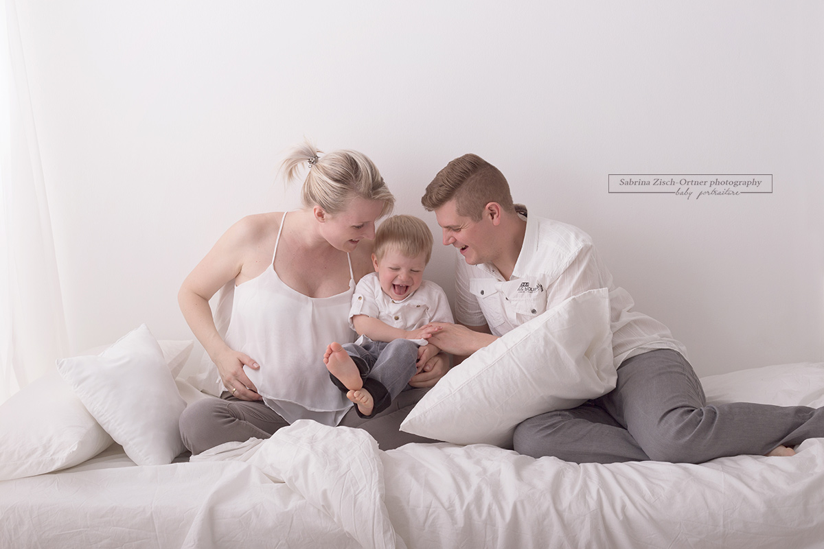 große Bruder lachend mit Eltern auf dem Studiobett beim Familien Babybauchfotoshooting