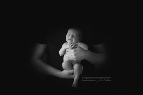 wunderhübsches schwarz weiß Bild welches Papas Hände zeigt in denen seine kleine Tochter mit einem lächeln aufrecht gehalten wird