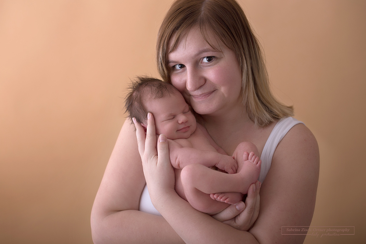 Mama und ihre 1 Wochen alte Tochter lächeln beide in die Kamera