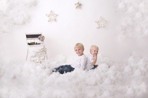 Geschwister in weiß gekleidet lachen im vorbereiteten Schnee Weihnachtssetup für die Weihnachtsminis