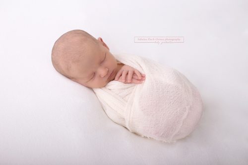 Neugeborene mit weißem Wrap umhüllt fotografiert auf Beanbag