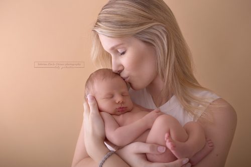 zärtliche Kuss einer glücklichen Mama beim Neugeborenenfotoshooting