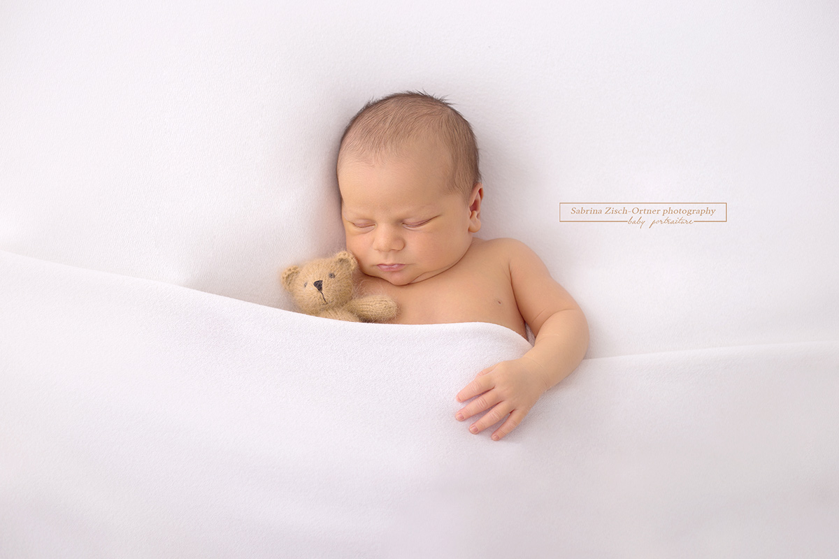Neugeborene Junge und kleine braune Teddybär kuscheln unter der Decke