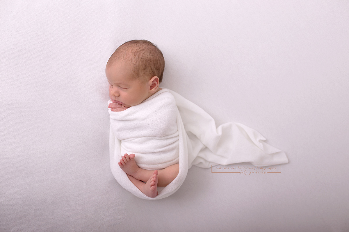 Neugeborener Junge in weißen Wrap für Fotoshooting gewickelt