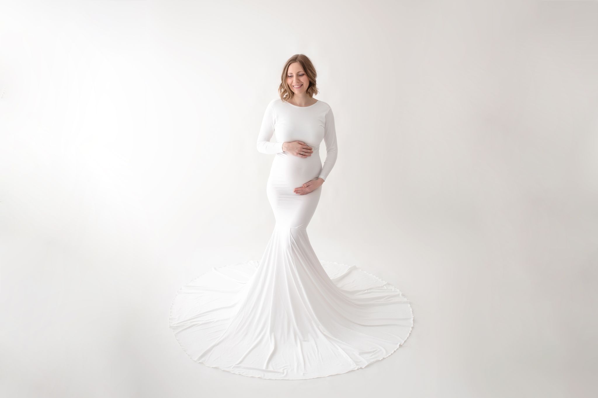 eine wunderhübsche Schwangere in einem weißen Kleid mit langer Schleppe bildet das Cover der Babybauchgalerie von Zisch-Ortner