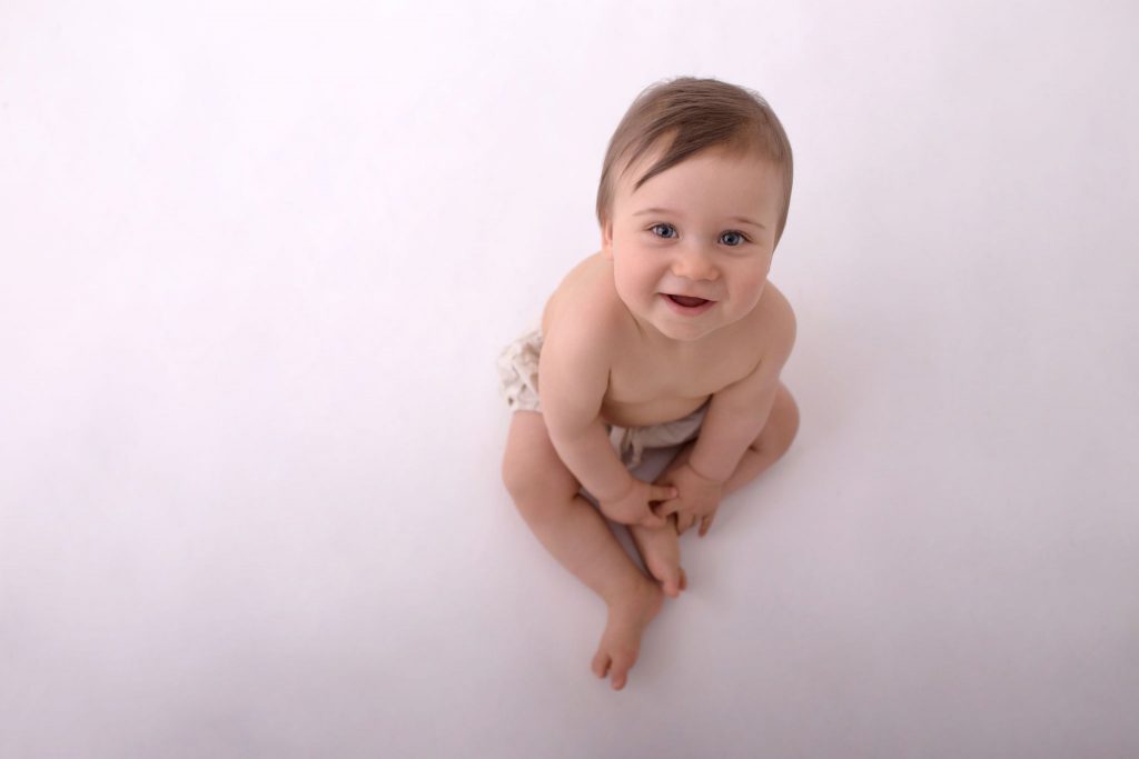 ein lächelnder 8 Monate alter Bub strahlt in die Kamera beim Shooting