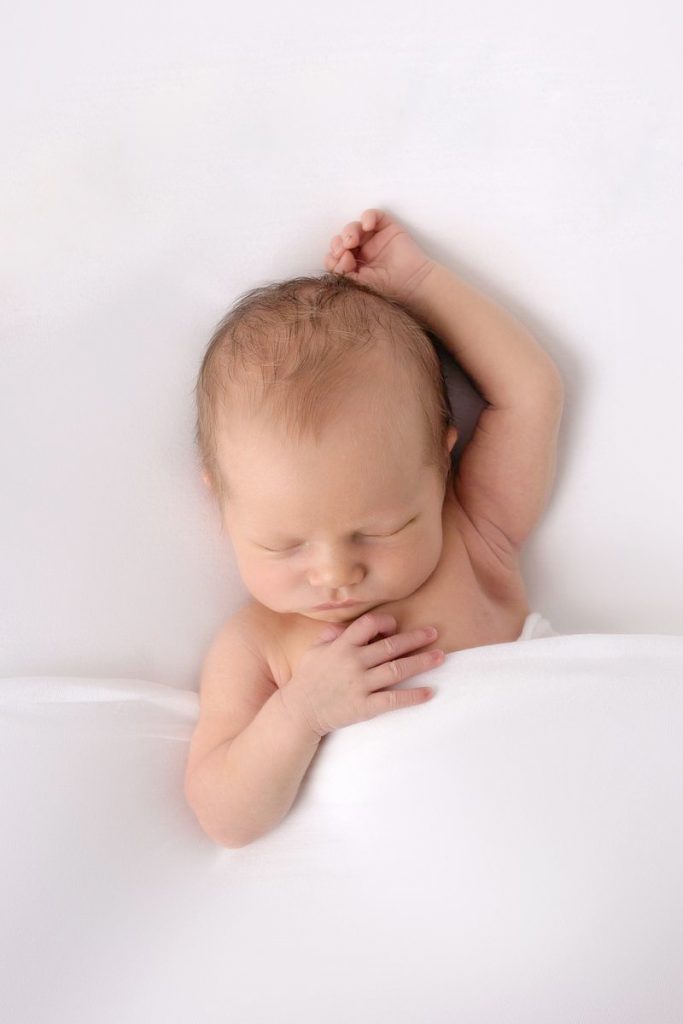 tief schlummernde Neugeborene liegt authentisch und natürlich bei seinem ersten Fotoshooting auf dem Beanbag