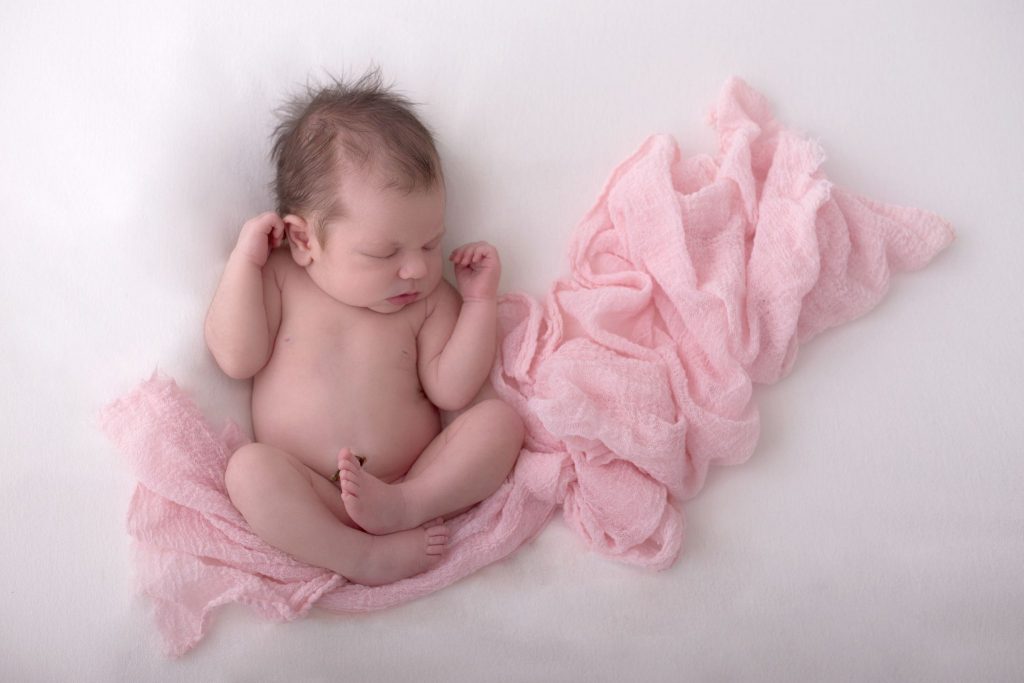 neugeborenes Mädchen liegt entspannt für ihr Fotoshooting auf einem rosa Tuch