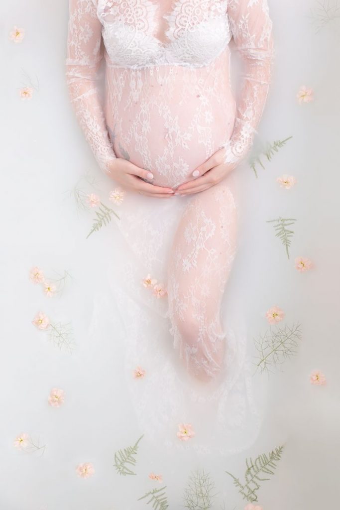 FAQ Milchbad Schwangerschafts Fotoshooting Bild zeigt Babybauch in rosa und grün dekorierter Badewanne und Spitzenkleid