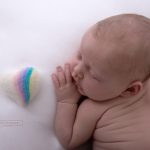 Filzherz mit kleinem Regenbogen liegt neben kleinem Neugeborenen