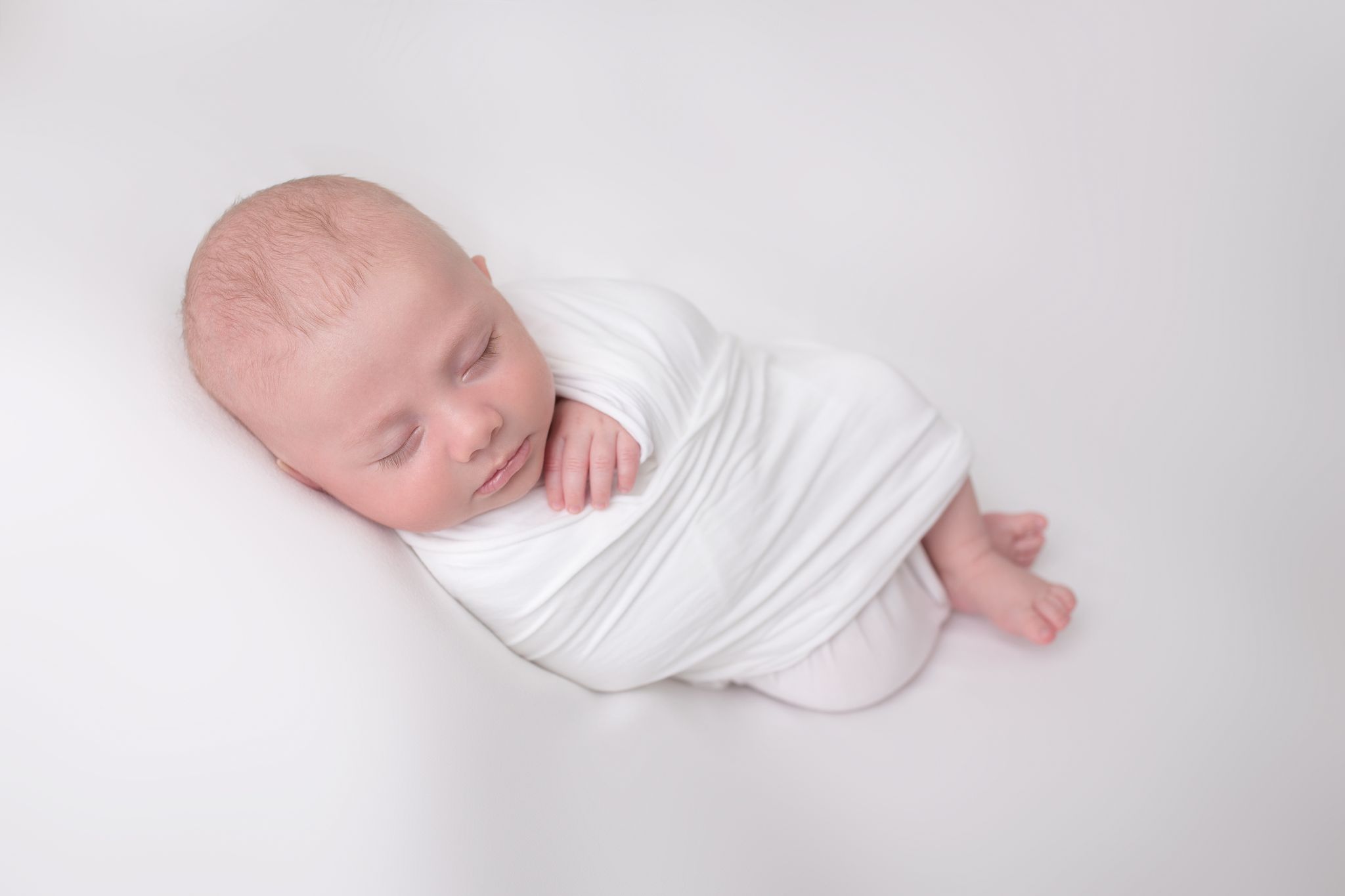 kleines Neugeborenes eingewickelt in weiß führt zu Blog der Babybauch und Familien Fotografin Sabrina Zisch-Ortner
