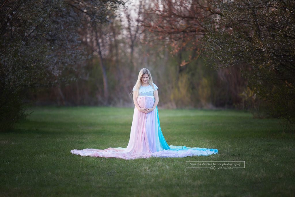 Schwangere im blauen Schwangerschaftskleid mit pastellfarbigen Regenbogenrock im Frühling