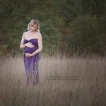 Schwangere mit Babybauchkugel im hohen Savannengras stehend