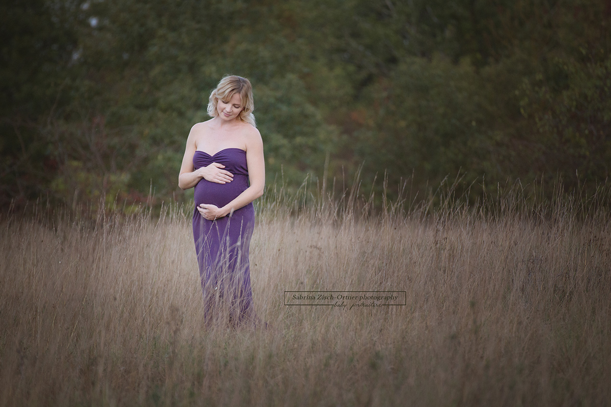 Schwangere mit Babybauchkugel im hohen Savannengras stehend