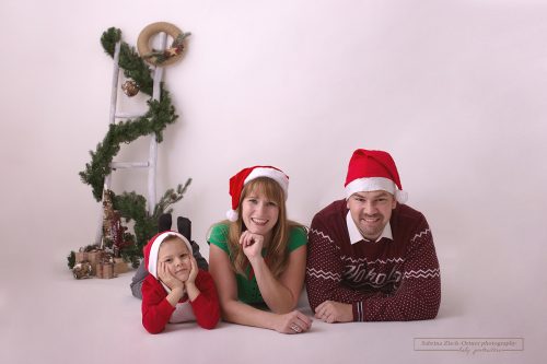 süßes liegendes Familienfoto der dreiköpfigen Familie mit Weihnachtsmützen