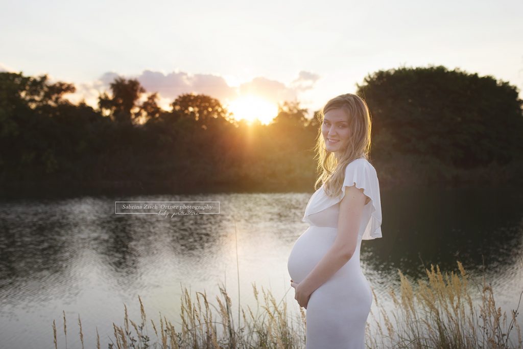 wunderhübsche Schwangere im weißen Kleid beleuchted von orangenen untergehenenden Sonne