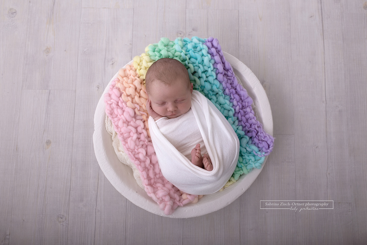 Baby auf Decke aus Regenbogenfarben in weißen Schalen