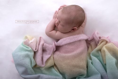 handgestrickte Decke in Regenbogenfarben ueber neugeborenen Kind