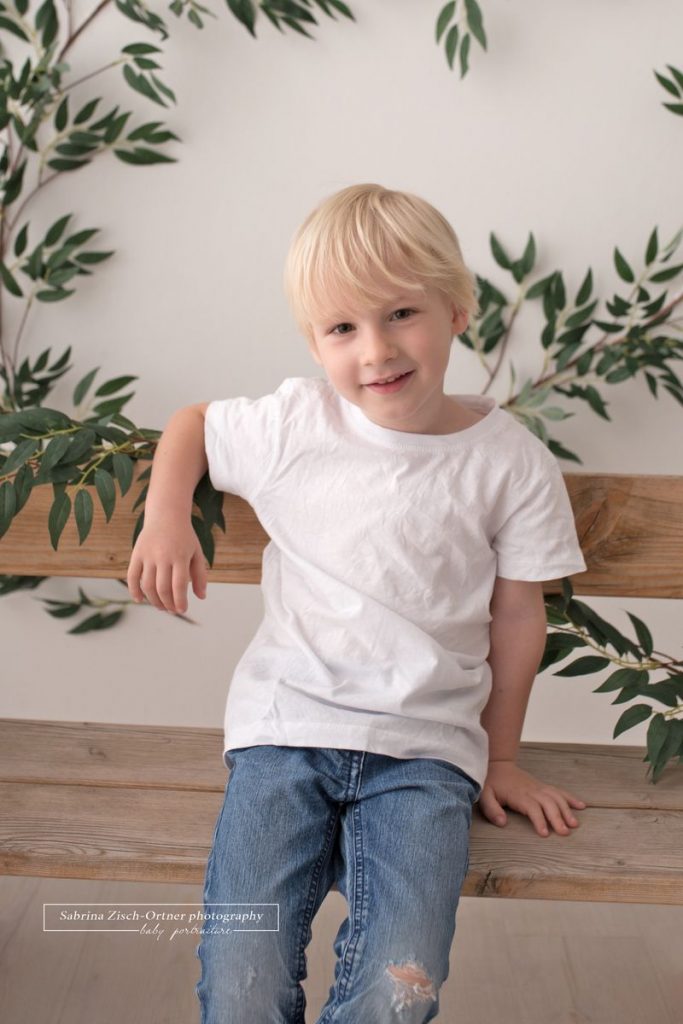 Vier jährige lehnt lässig und cool an der Holzbank in blauer Jean und weissem Tshirt für sein Fotoshooting
