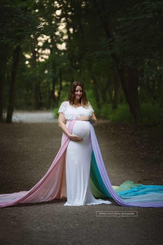 Schwangere im Wald stehend für ihr Fotoshooting mit ihrem Regenbogenbaby im Bauch