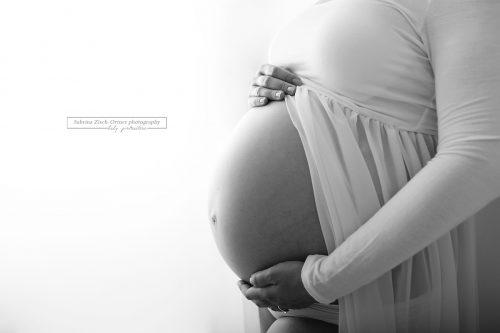 kugelrunder Babybauch in Nahaufnahme umrundet von Schwangerschaftskleid