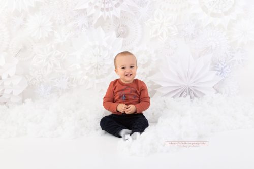 Bub in Schnee aus Watte vor Schneeflockenwand aus Papier für professionelle Weihnachtsfoto