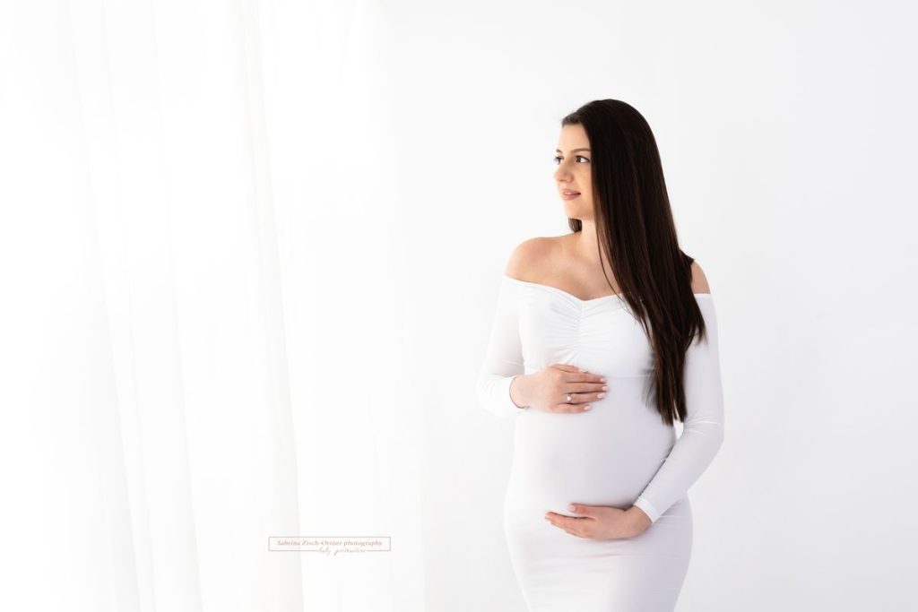 Schwangere im engen weißen Babybauchkleid mit offenen langen schwarzen Haaren