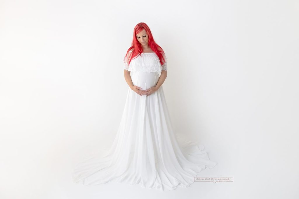 Studiobabybauch Fotoshooting in weißem Kleid mit weißem Tüllrock und roten Haaren