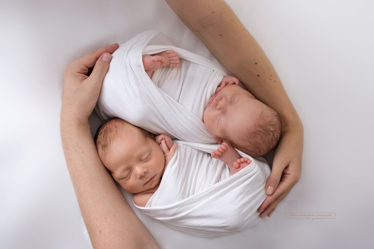 Zwillinge beim Neugeborenenshooting in den Händen der Eltern