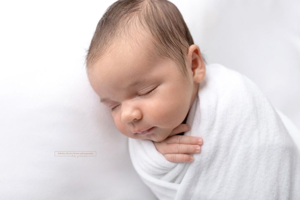Baby bei ihrem Neugeborenenshooting in weiß gewickelt