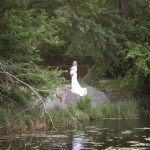 Babybauch Outdoorshooting im weißen Kleid von grüner Natur und Wasser umgeben