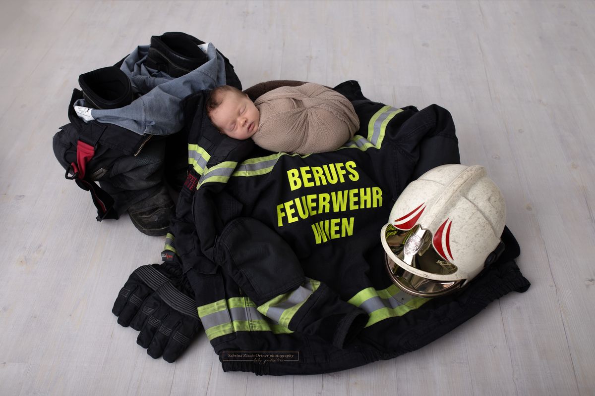 Babyfotos einer Feuerwehrtochter die auf Feuerwehrgewand des Papas liegt