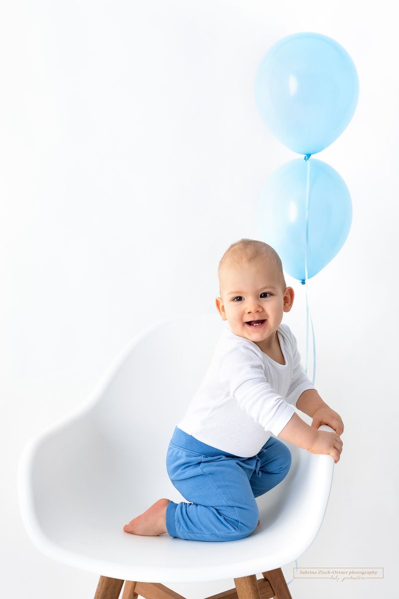Happy Birthday zum Ersten Geburtstag mit blauen Luftballons und weißem Sessel