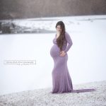 Schwangere im lila Babybauchkleid vor zugefrorenen und verschneiten See