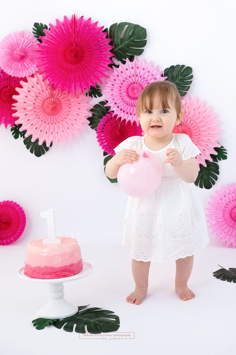 einjährige Mädchen stehend mit Luftballon vor Cake Smash Dekoration
