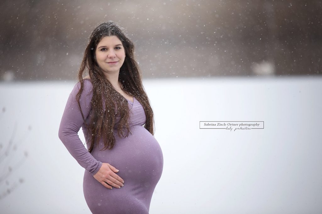 glücklich lächelnde Schwangere in handgeschneiderten Babybauchkleid bei ihren Winter Outdoor Fotos
