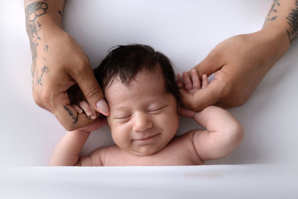 grinsendes schlafendes neugeborenes Maedchen mit Mamas Händen