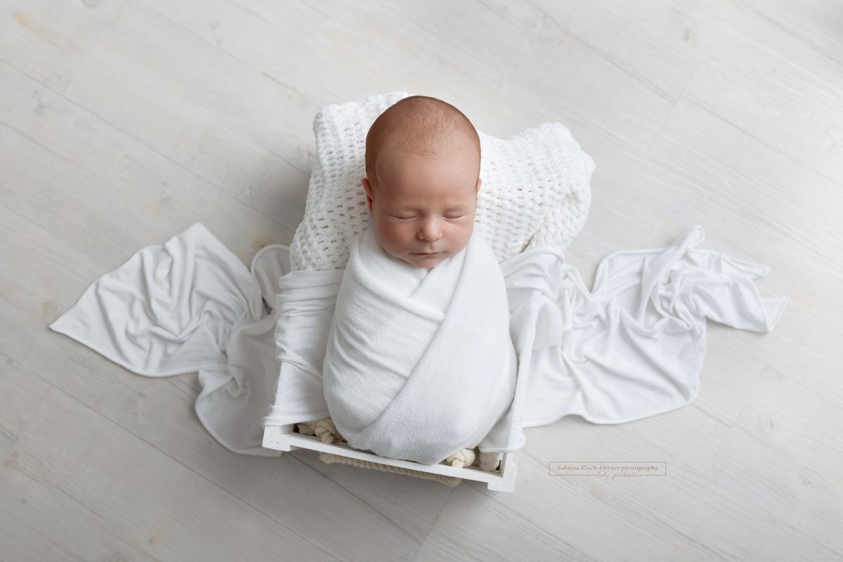neugeborener Junge in weißen Bett mit weißen Tüchern beim Fotoshooting