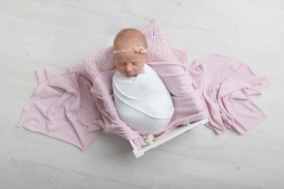 neugeborenes Maedchen in weißen Kiste mit rosa Tuch und Haarband