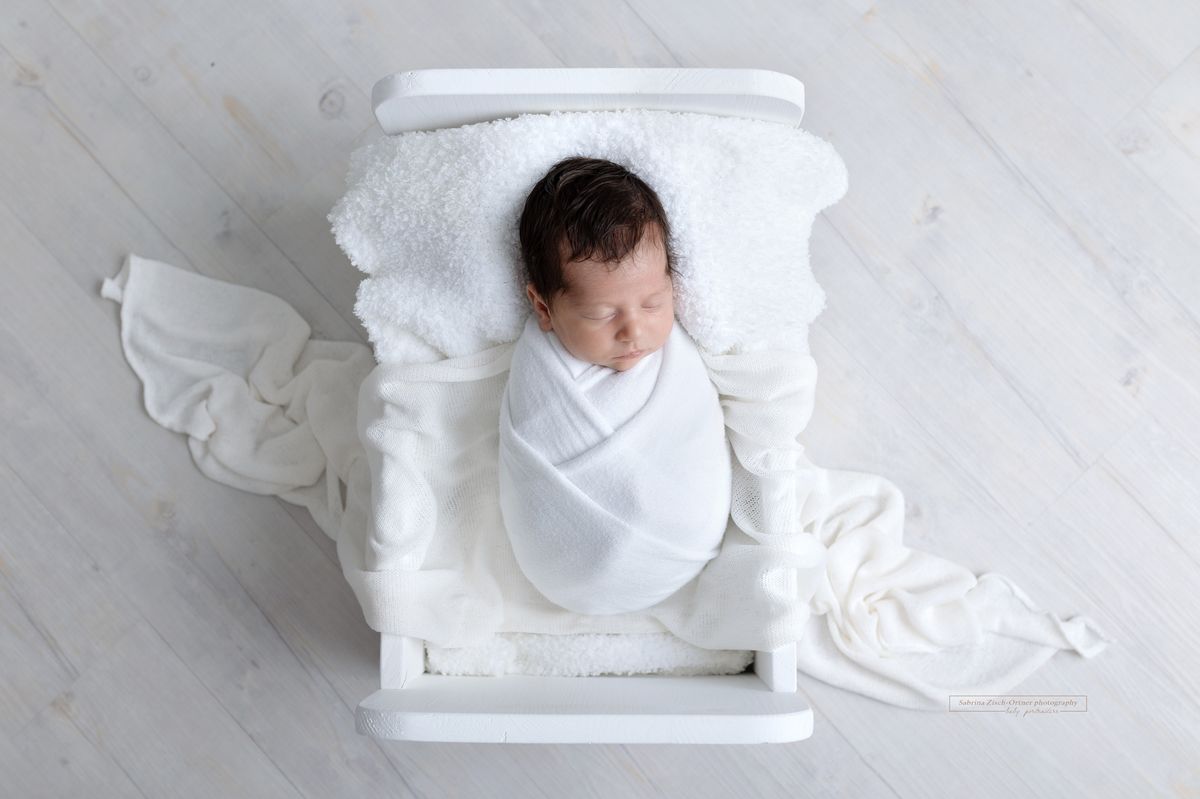 neugeborenes Maedchen liegt in weißen Bett für ihre Fotos