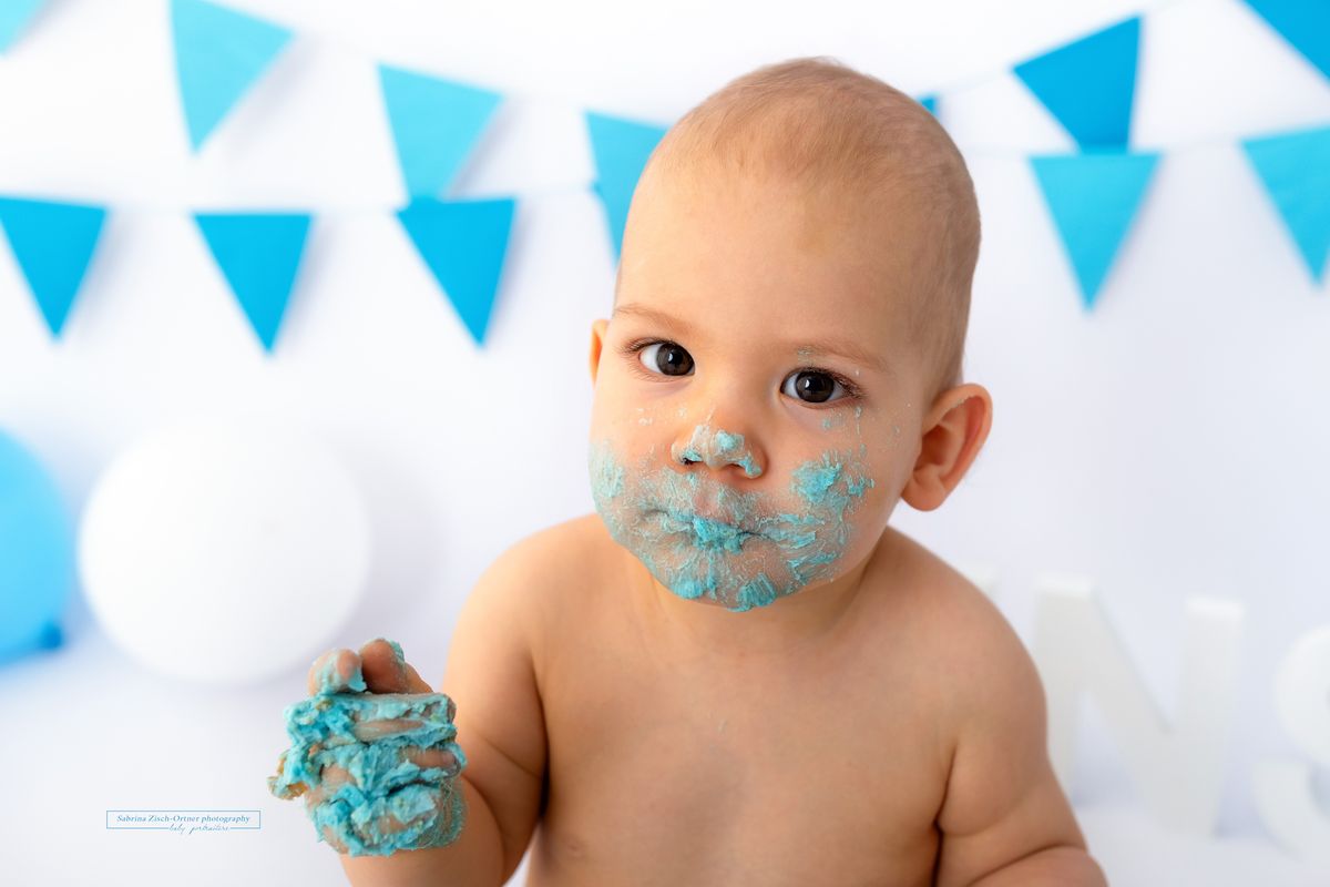 Baby voll mit Buttercreme vom Cake Smash Fotoshooting