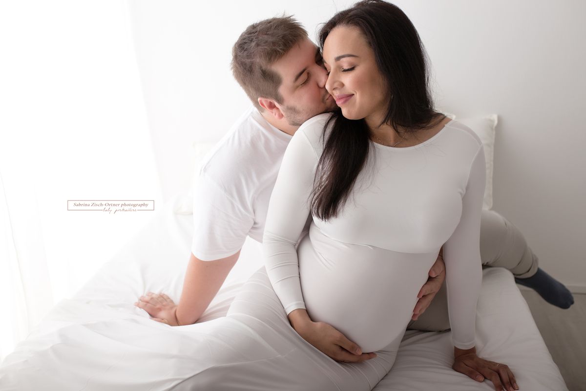 Werdenden Eltern kuscheln während dem Babybauchshooting am Bett