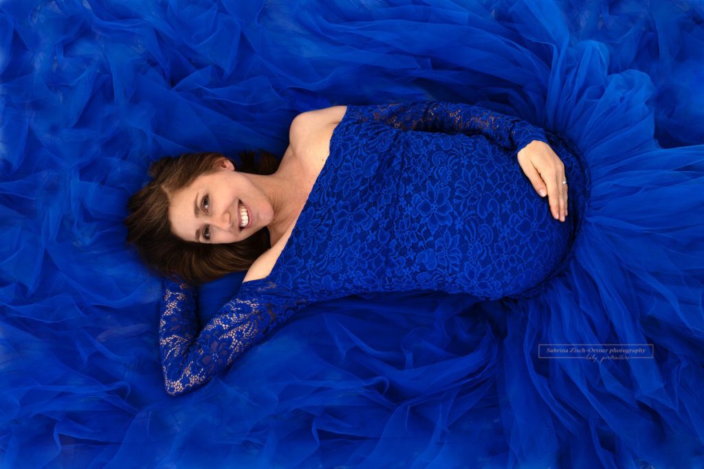 Bald Mama liegt im Studio auf ihrem Babybauchkleid in Blau