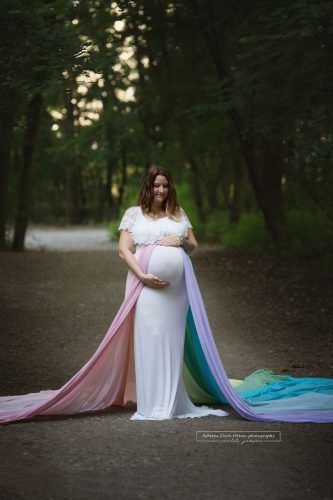 Schwangere im Wald stehend für Fotoshooting mit ihrem Regenbogenbaby im Bauch