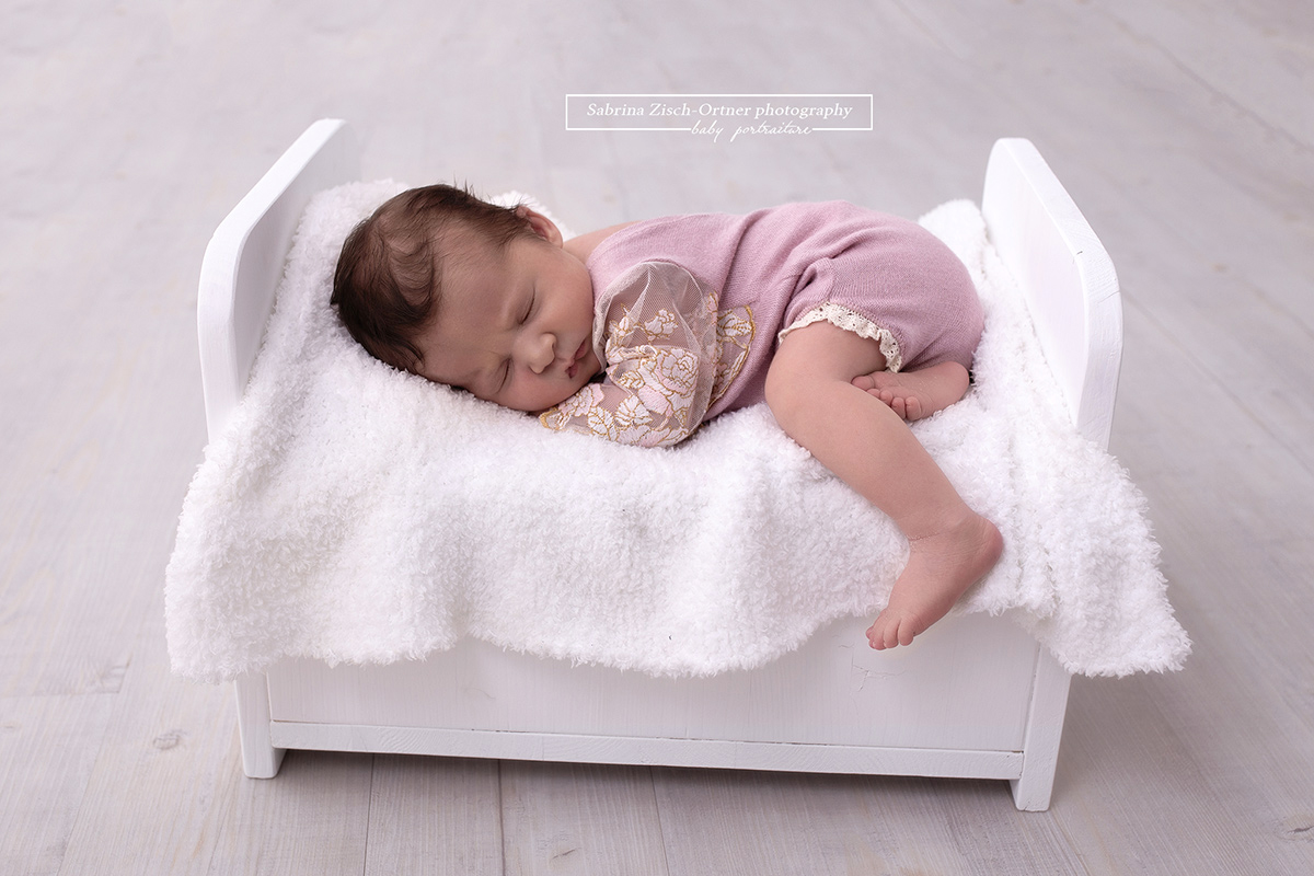 neugeborene Mädchen in Rosa Outfit schlafend in einem kleinen Bettchen