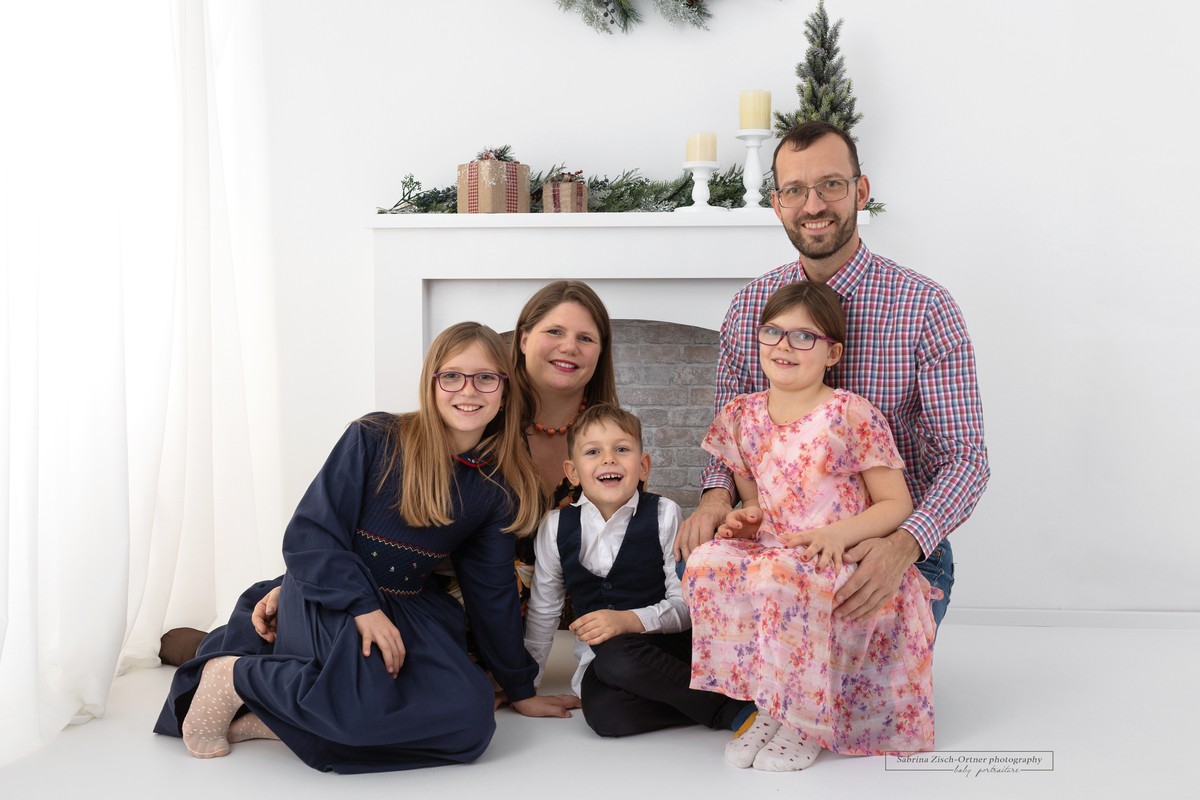 sitzendes Familienfoto vor weihnachtlich dekorierten Kamin